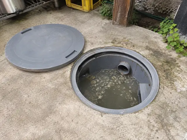 Cámara desgrasadora abierta en el patio de servicio de un restaurante, con grasa flotando en el agua